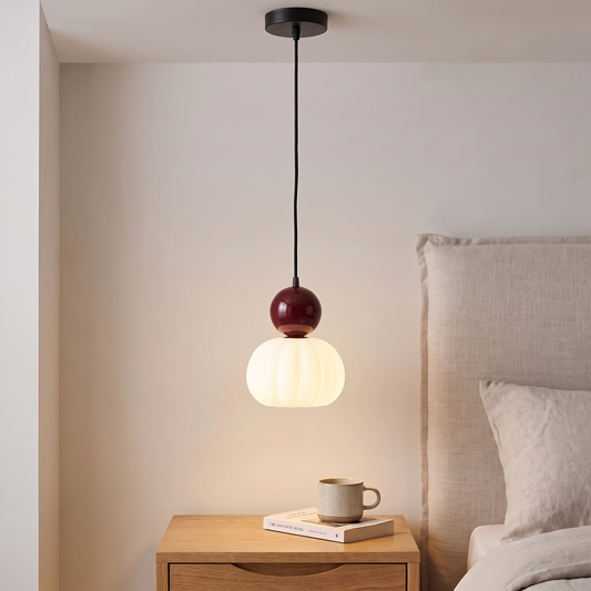 Pumpkin ribbed glass pendant light with red ball knob, lit at a bedside
