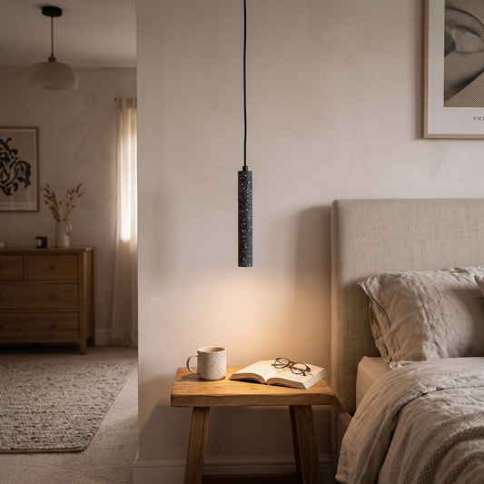 Black terrazzo tube pendant light lit at a bedside