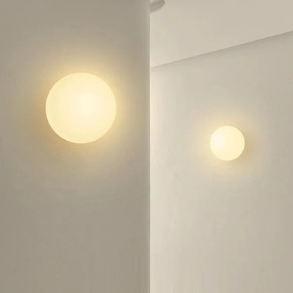 Two milky glass globe wall lights lit on a pale bathroom wall
