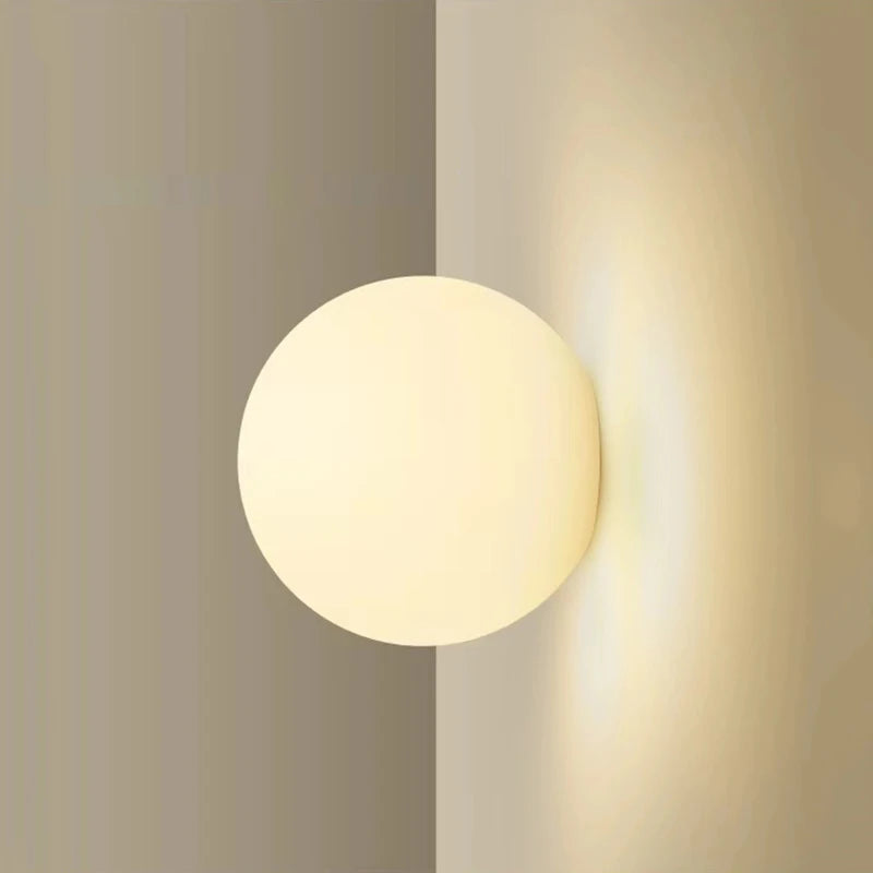 Milky glass globe wall light glowing against a warm neutral wall
