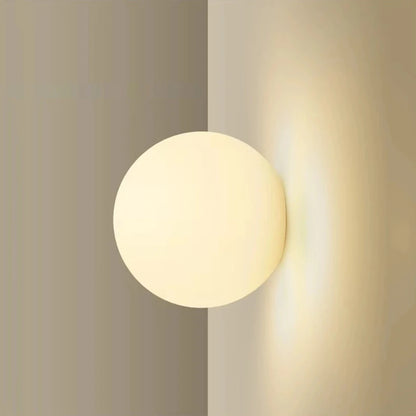 Milky glass globe wall light glowing against a warm neutral wall