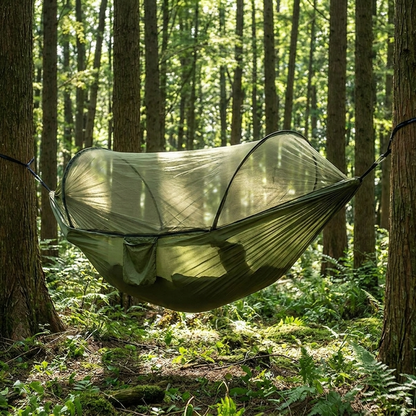 Camping hammock with mosquito net hung between trees in woodland setting