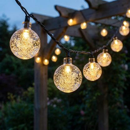 Solar crystal globe string lights glowing warm yellow along a garden pergola at dusk