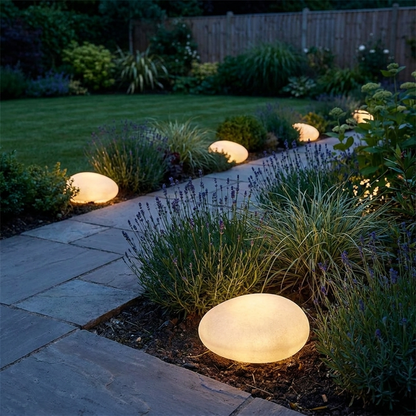 Frosted solar pebble lights glowing in garden planting at dusk