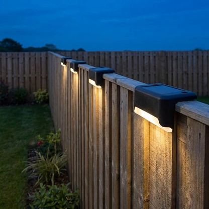 Black solar deck lights with warm white glow on a fence top