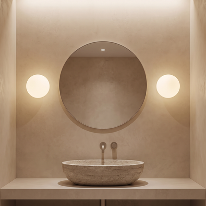 Pair of milky glass globe wall lights either side of a round bathroom mirror above a stone basin