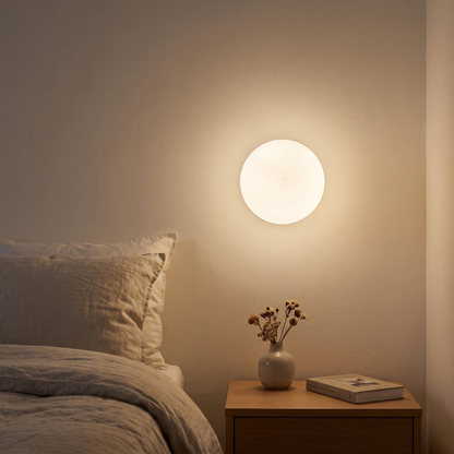 Milky glass globe wall light glowing at bedside above a wooden nightstand