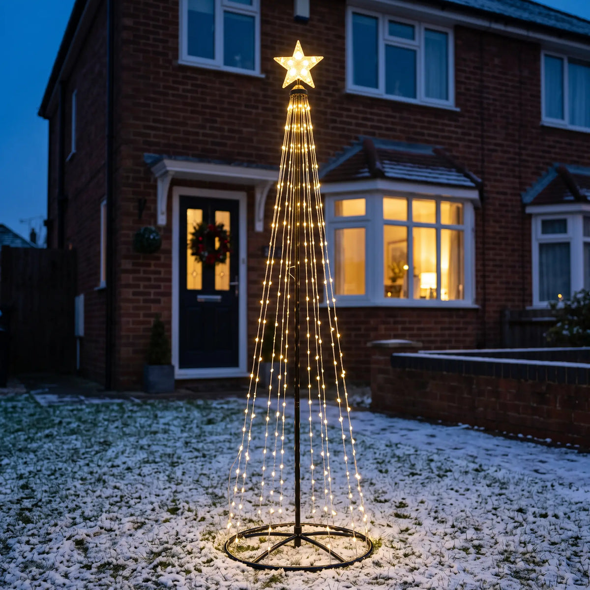 Warm white rotating LED cone outdoor Christmas tree with star in a front garden
