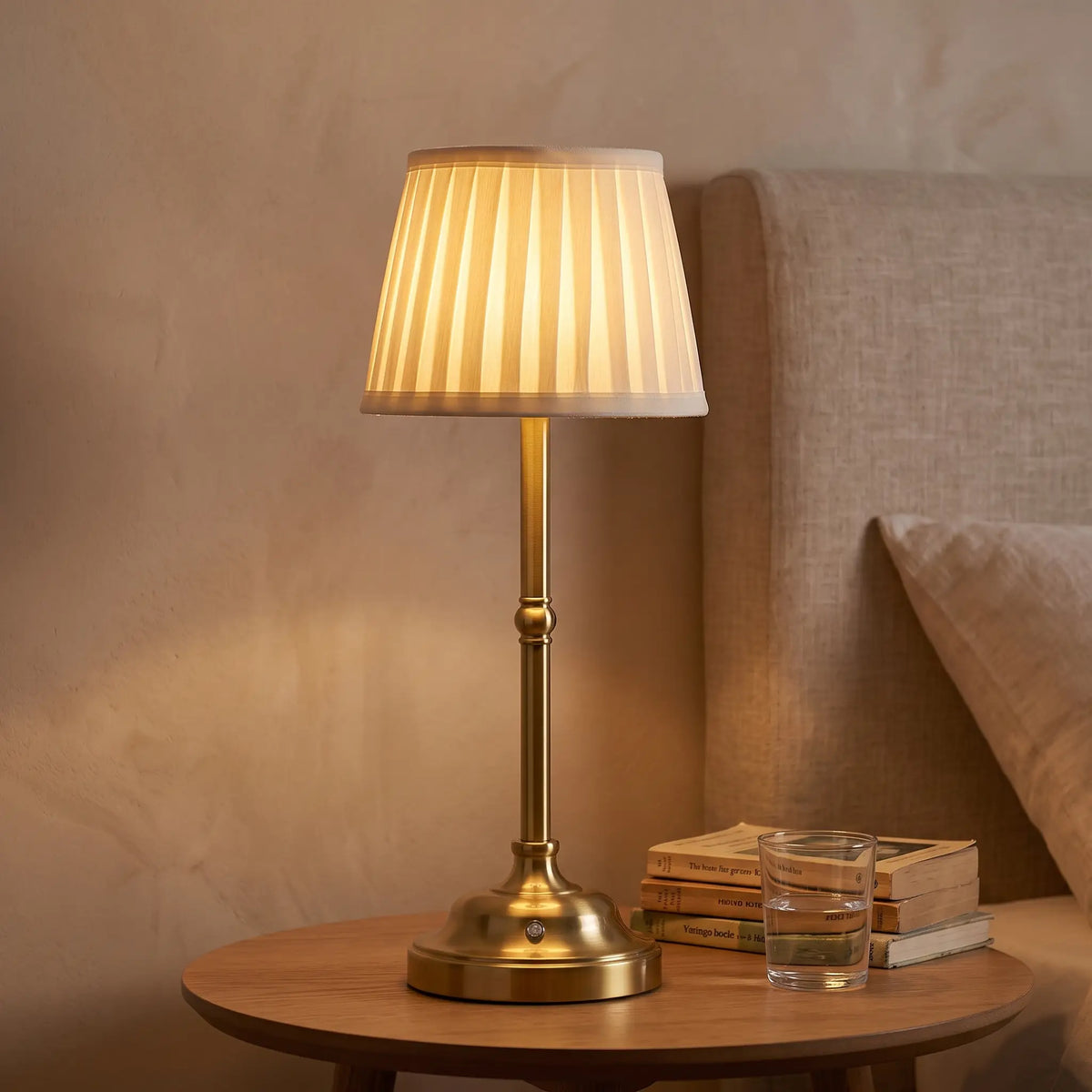 Brass cordless table lamp with cream pleated shade on a bedside table