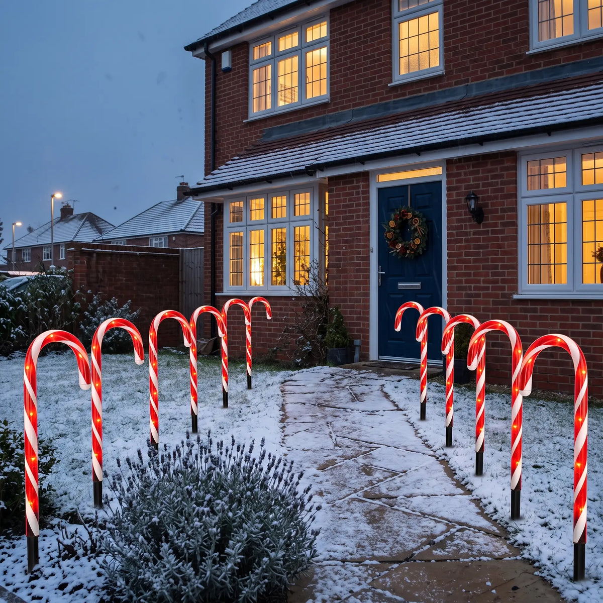 Red and white candy cane path lights lining a snowy front garden path