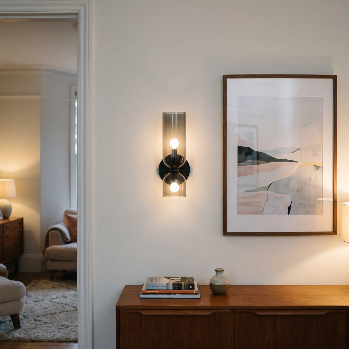 Smoke grey glass cylinder wall sconce beside a framed print, lit
