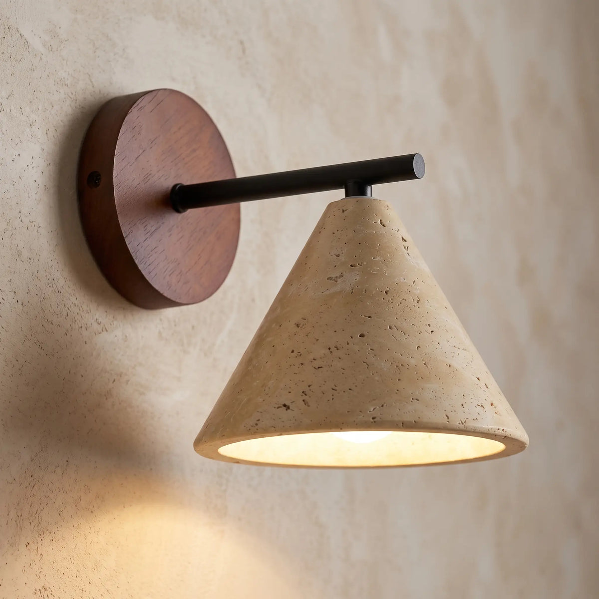 Close-up of the travertine cone shade, wooden backplate and black arm, lit