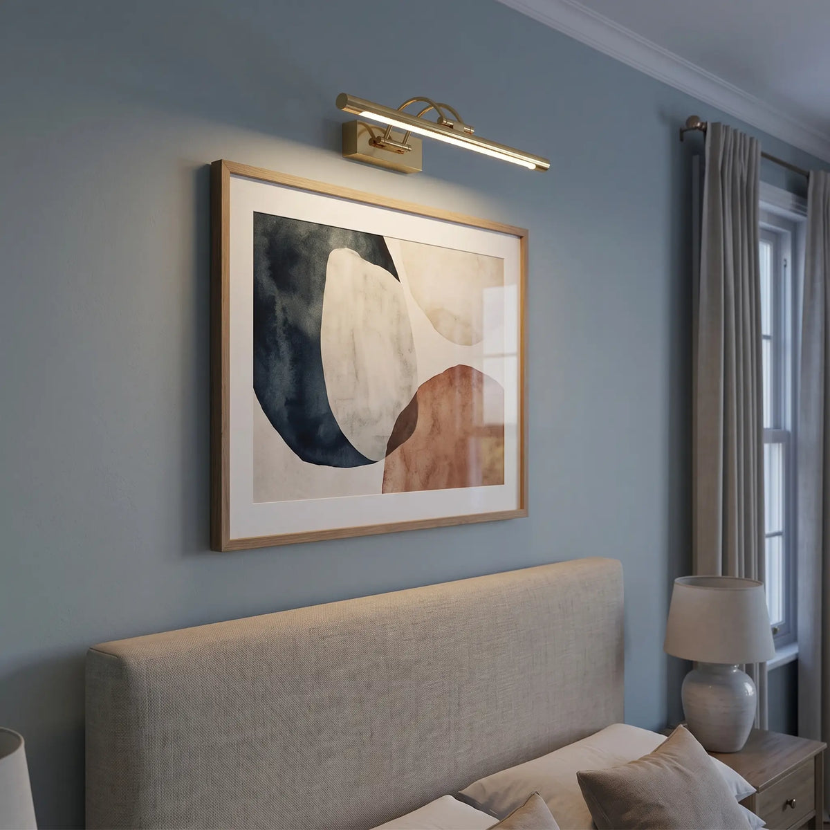 Brass picture light above artwork over a bed, lit
