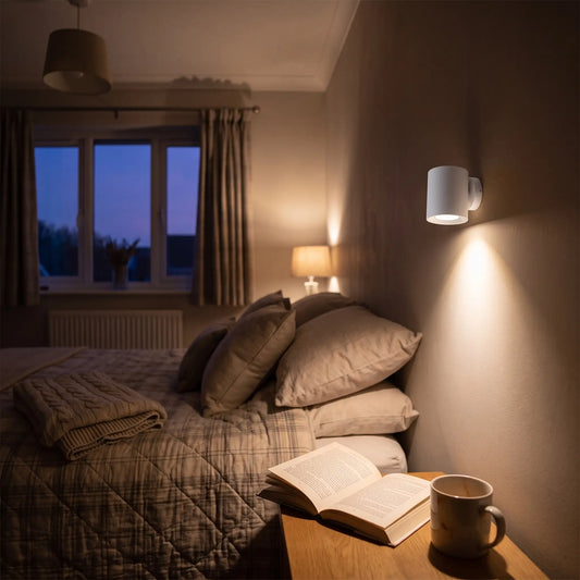 White rechargeable wall spotlight beside a bed shining down onto a book
