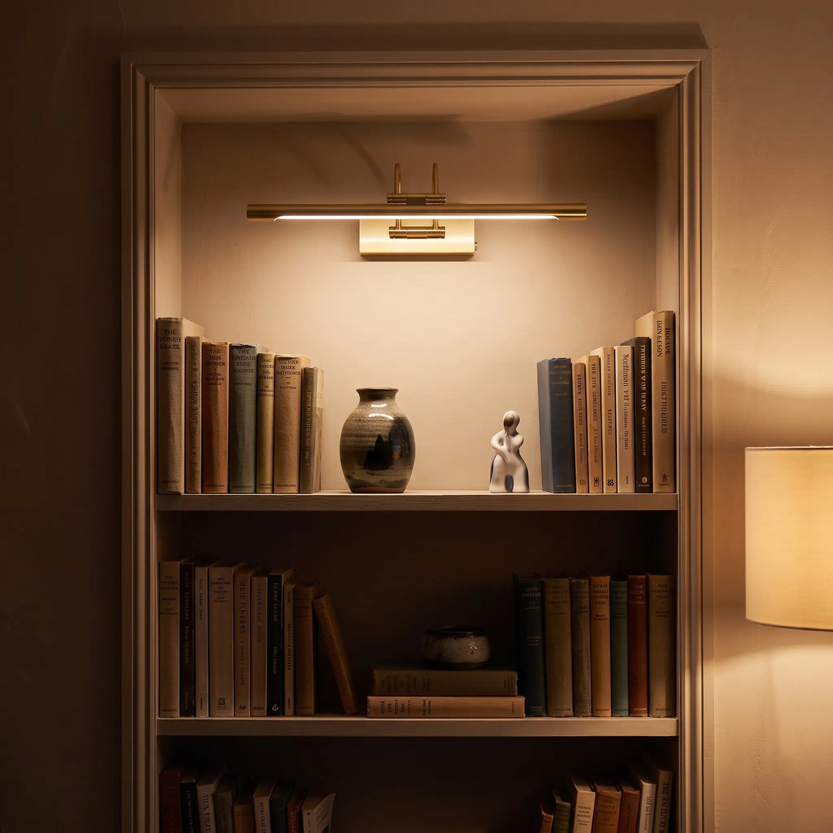 Brass picture light above an alcove bookshelf, lit