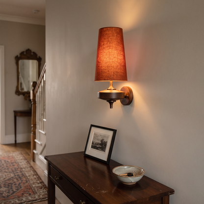 Rust red fabric wall light with tall shade, lit above a hallway console table
