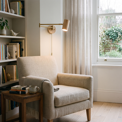 Natural wood swing arm wall light with brass arm above a linen armchair