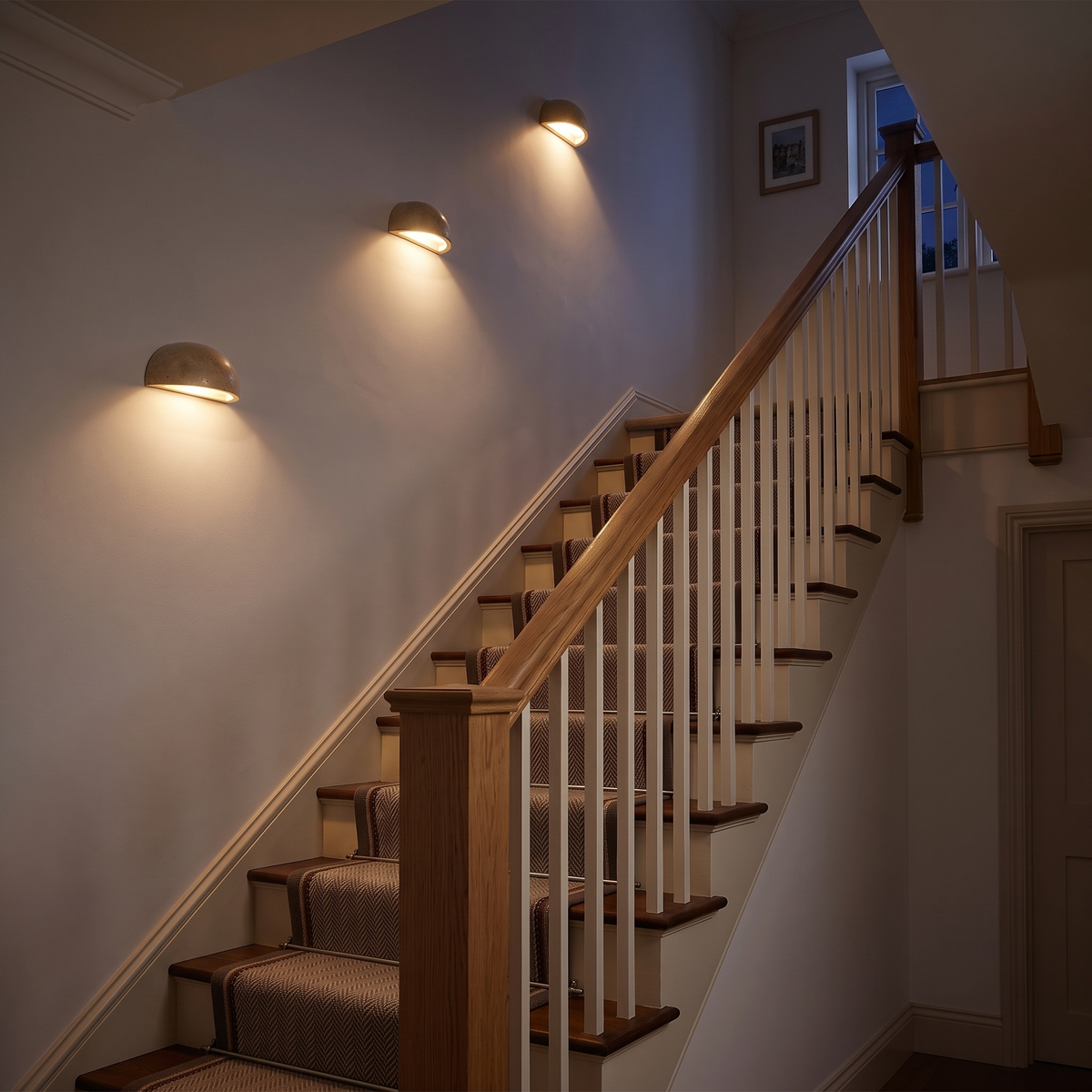 Three half moon travertine wall lights along a staircase, each lighting downwards