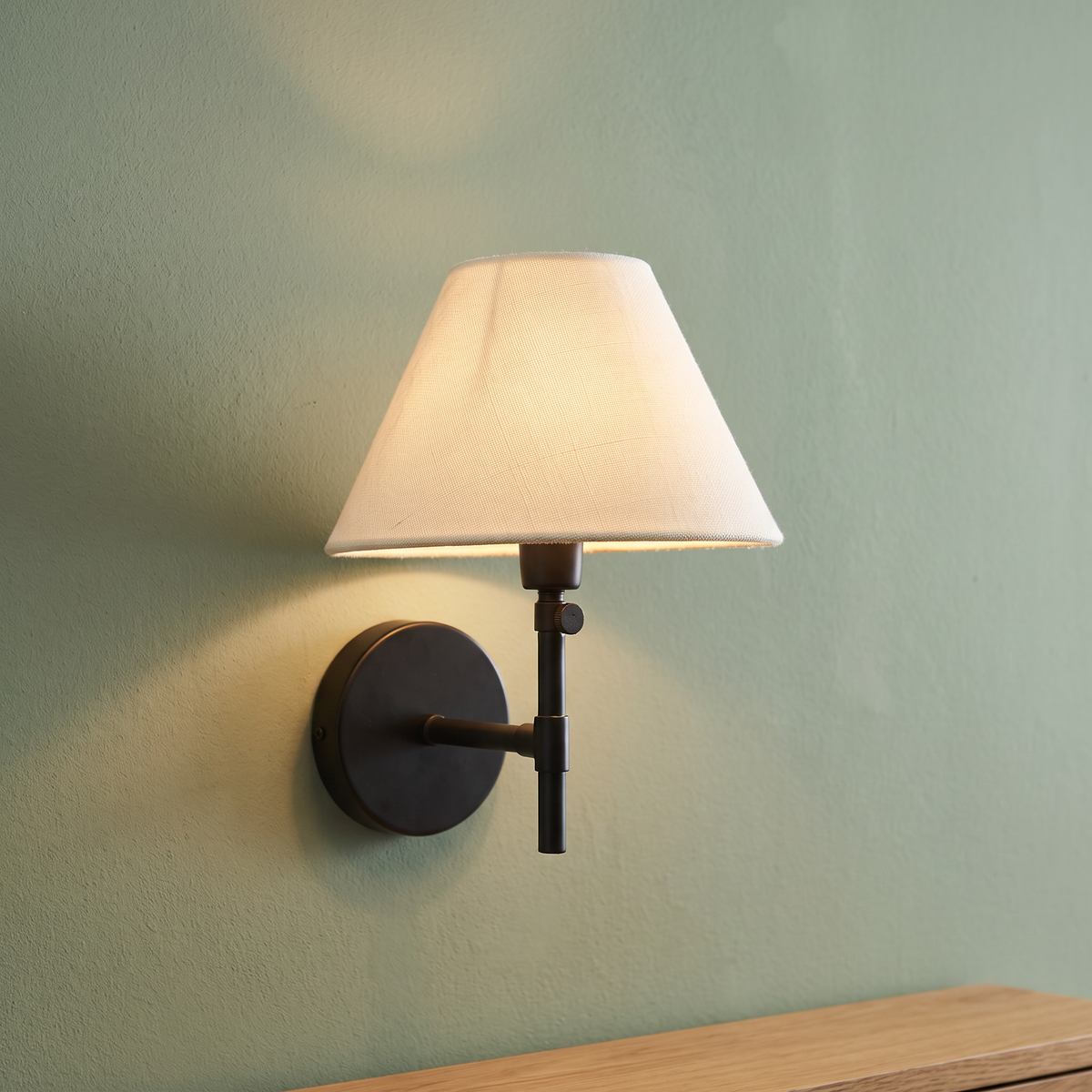 White linen coolie shade wall light with black arm, close-up in a hallway
