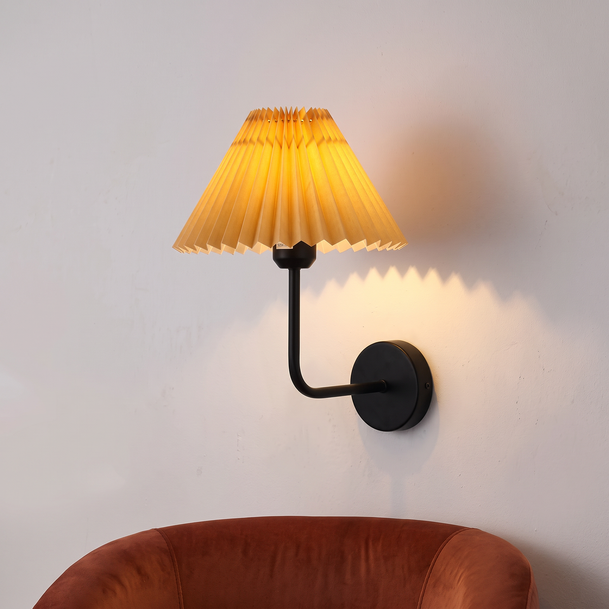 Pleated fabric wall light with black arm and apricot shade, close-up beside an armchair