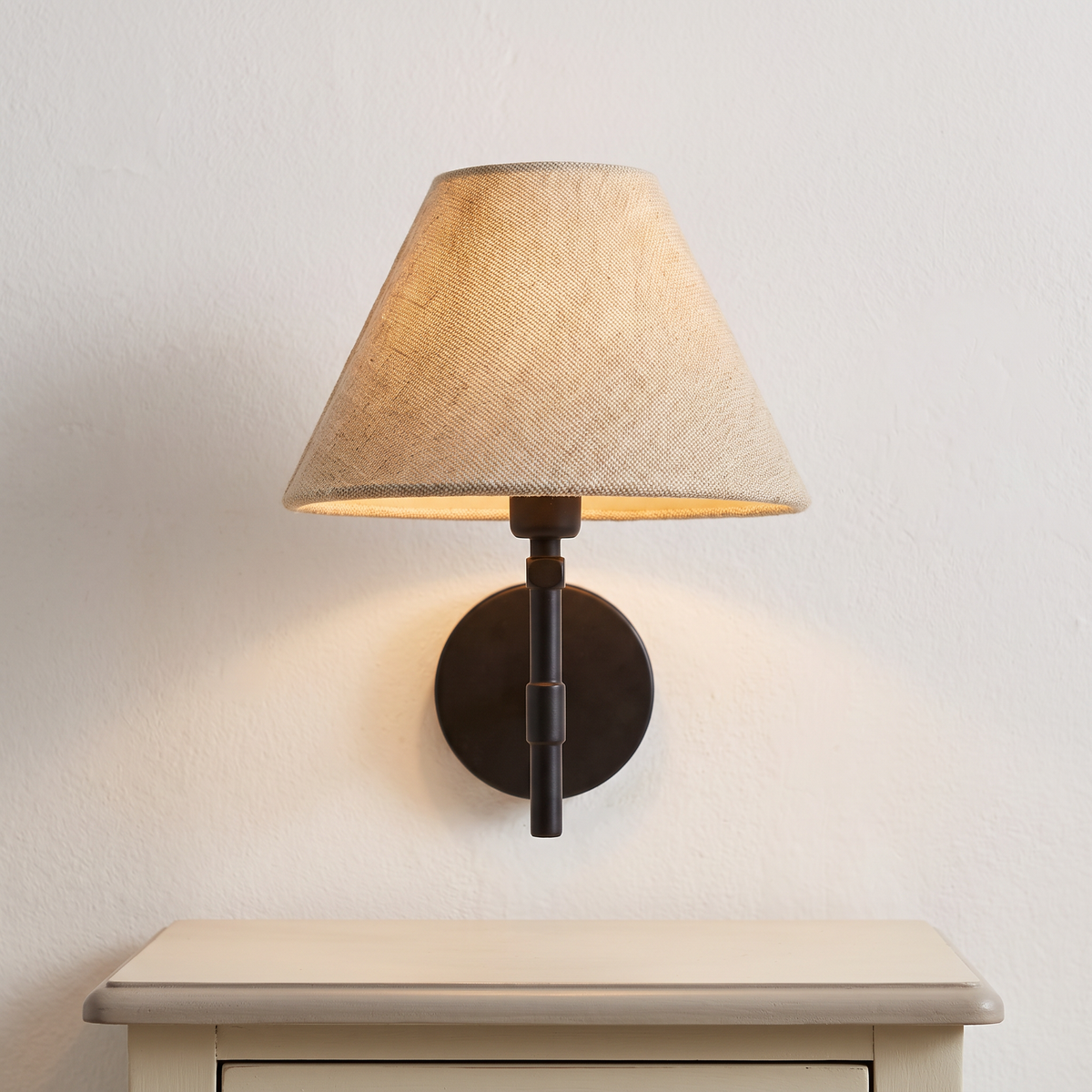 Beige linen coolie shade wall light with black arm, close-up above a bedside table