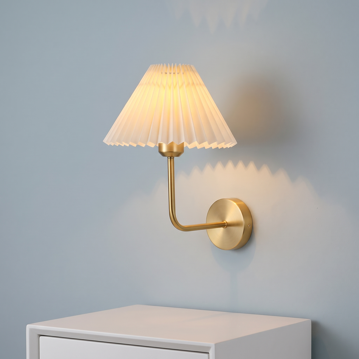 Pleated fabric wall light with brass arm and white shade, close-up above a bedside table