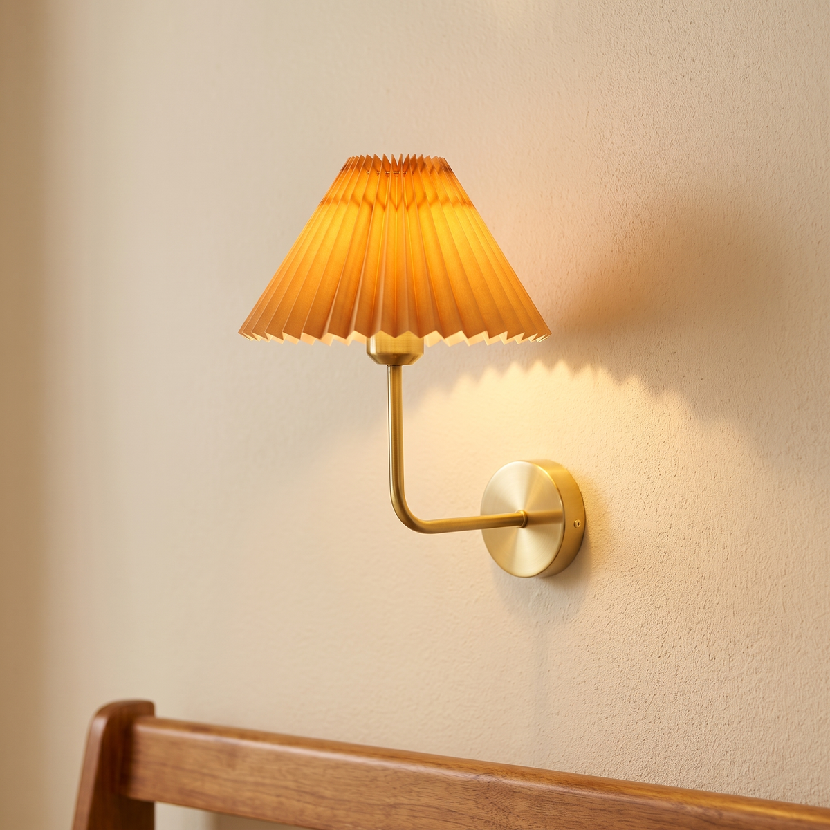 Pleated fabric wall light with brass arm and apricot shade, close-up in a hallway