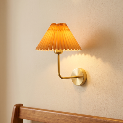Pleated fabric wall light with brass arm and apricot shade, close-up in a hallway