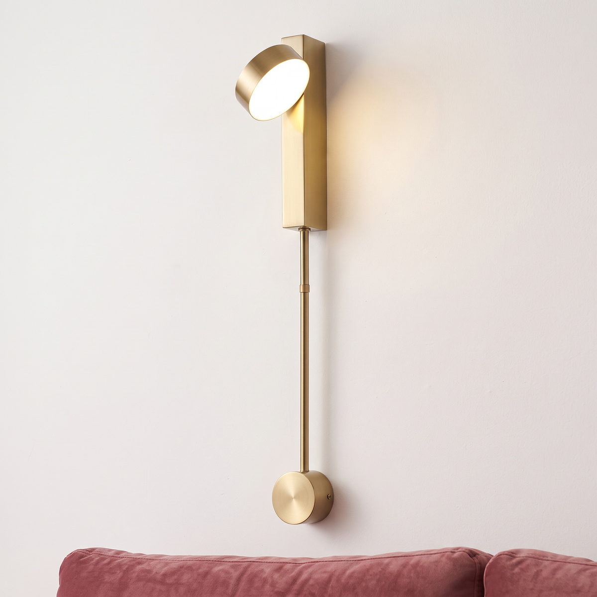 Gold rotating-head rod LED wall light, close-up beside a sofa