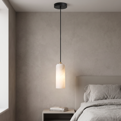 Natural marble cylinder mini pendant light with black canopy and cord, lit beside a bed