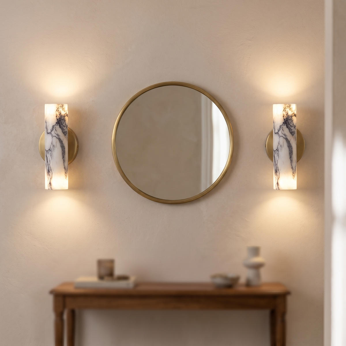 Pair of natural marble up and down wall lights either side of a round brass mirror in a hallway
