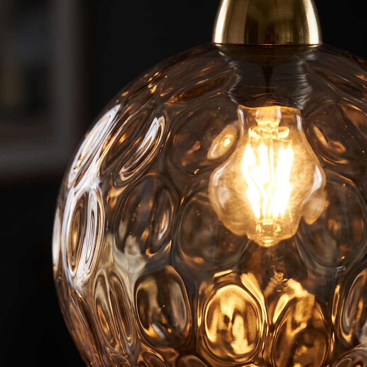 Close-up of the dimpled water-ripple texture on the amber glass globe pendant, lit