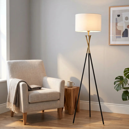 Tripod floor lamp with white drum shade beside an armchair