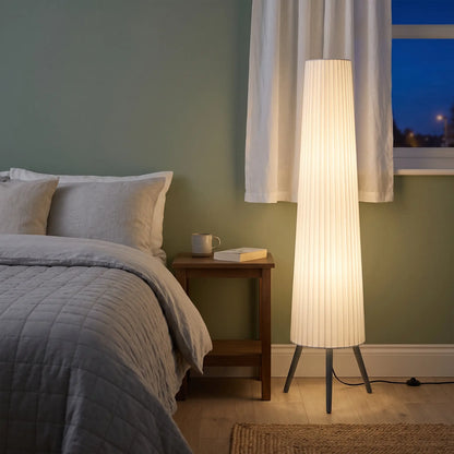 Tripod floor lamp with tall white fabric shade in a bedroom