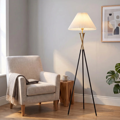 Tripod floor lamp with white pleated shade beside an armchair