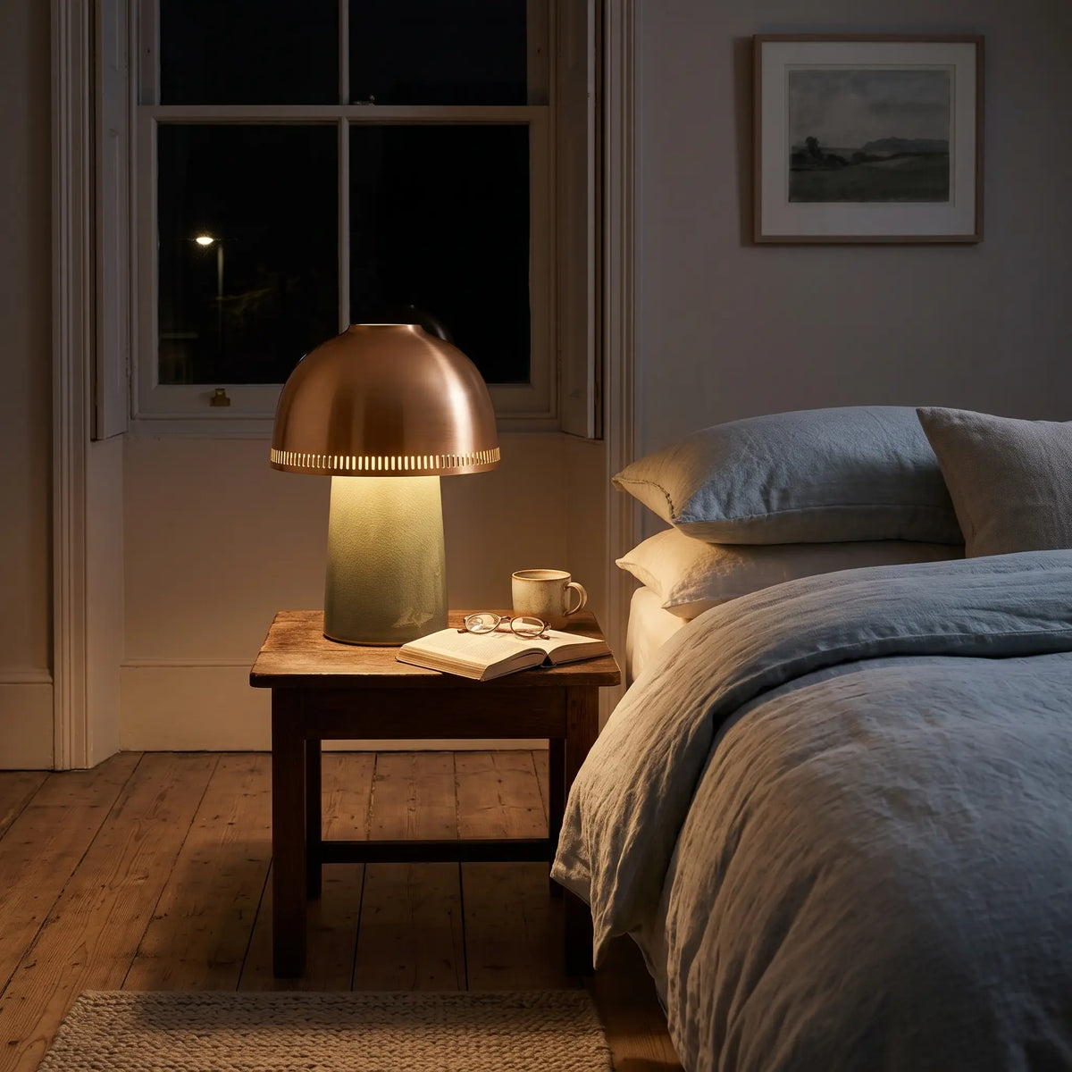 Sage green ceramic lamp with copper shade on a bedside table