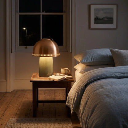 Sage green ceramic lamp with copper shade on a bedside table
